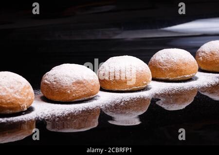 Baking on a black background. White buns sprinkled with powder and flour. Stock Photo