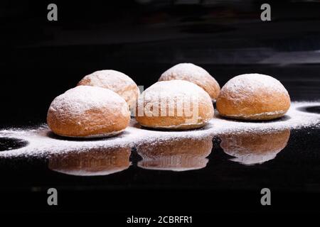 Baking on a black background. White buns sprinkled with powder and flour. Stock Photo