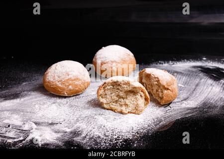 Baking on a black background. White buns sprinkled with powder and flour. Stock Photo
