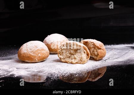 Baking on a black background. White buns sprinkled with powder and flour. Stock Photo