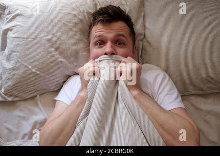 Man hiding in bed under the blanket at home Stock Photo