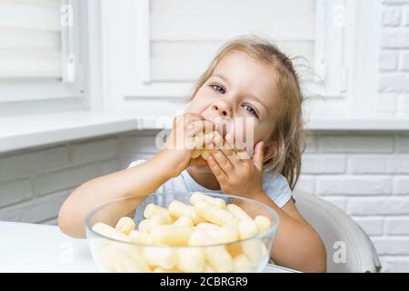 cute little girl puts a lot of corn sticks in her mouth Stock Photo