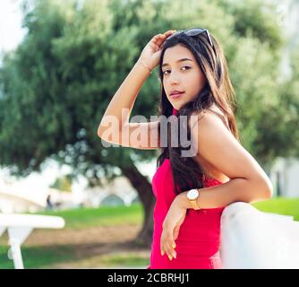 young girl brunette Latina with long black hair and black eyes, wearing a red dress, leaning on a white railing. copy space Stock Photo