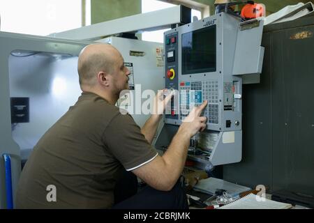 At the production hall. Engineer sitting in front of a control panel of CNC milling machine programming it Stock Photo