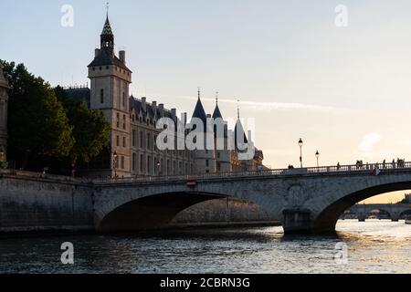 The conciergerie and the bridge Pont au Change seen from the seine river at sunset. Illuminated facade of medieval building. Stock Photo