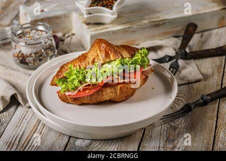 Croissant with Parma ham, red pesto cheese, tomato and fresh salad on a white plate. Morning food still life. Delicious breakfast concept Stock Photo