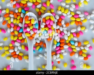 Multi colored fennel sugar candy in spoons and scattered as background, texture Stock Photo