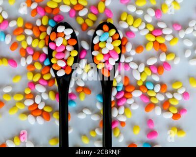 Multi colored fennel sugar candy in spoons and scattered as background, texture Stock Photo