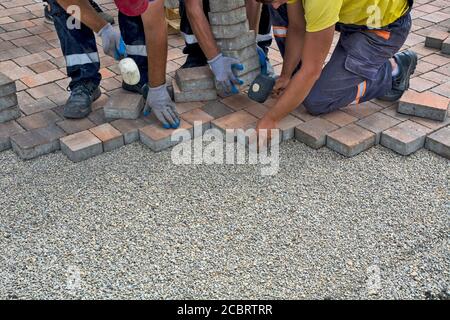 Masters lay and install floor bricks on a public surface. The base is small stone and they fit concrete decorative pieces of brick. Stock Photo