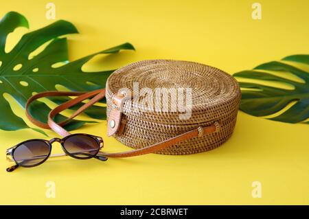 Handwoven Boho Bali Round Ata Rattan Beach Bag With Button Clip on a yellow and turquoise background Stock Photo