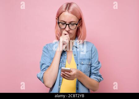Sad woman with dyed pink hair looking at her mobile phone Stock Photo