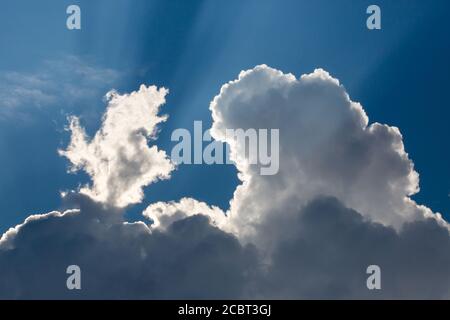 Sunbeams streak a deep blue sky behind dramatic cumulus clouds. Stock Photo