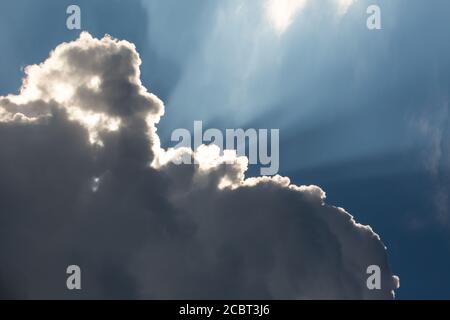 Sunbeams streak a deep blue sky behind dramatic cumulus clouds. Stock Photo