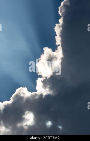 Sunbeams streak a deep blue sky behind dramatic cumulus clouds. Stock Photo