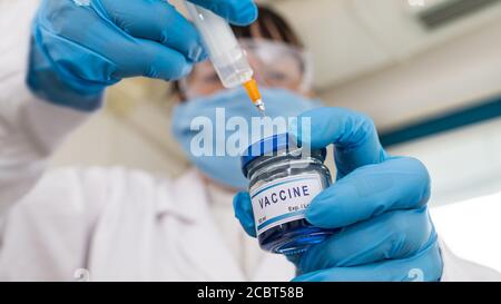 Laboratory assistant holding syringe, new coronavirus vaccine in glass bottle. Closeup of medical equipment. Hands in blue gloves. Scientific research. Stock Photo