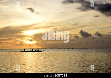 A team of outrigger canoe paddlers at sunset on the peaceful waters of Tumon Bay, Guam, Micronesia Stock Photo