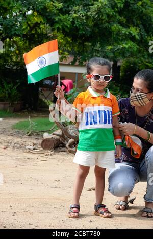 An adorable girl dressed as tricolor and written INDIA over it, holding national tricolour flag, wearing cloth mask celebrating Indian independence day in national capital Delhi amidst Covid-19 coronavirus pandemic  outbreak  in the year of 2020 Stock Photo