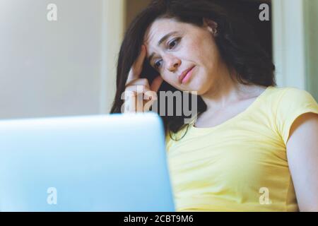 Distracted from work worried young woman sitting on couch with laptop, thinking of problems. Pensive unmotivated lady looking at laptop, feeling lack Stock Photo