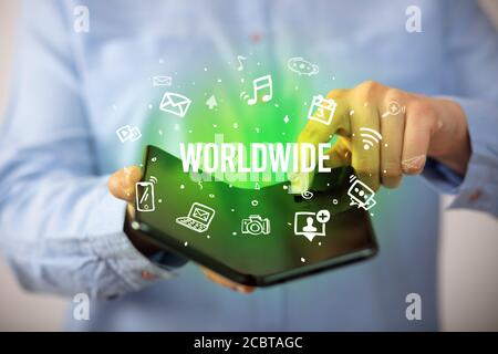 Businessman holding a foldable smartphone with WORLDWIDE inscription, social media concept Stock Photo