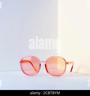 Modern pink sunglasses in front of the corner of the wall background with copy space. Product photograph of minimalist concept with room for text, fro Stock Photo