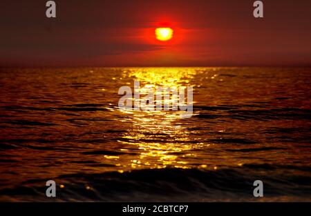 Sunset by the sea. Spectacular fiery red sun above the background waves. Stock Photo