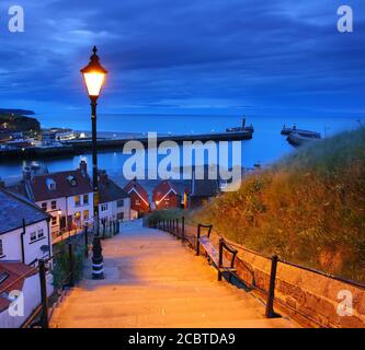 Image showing the 199 steps to whitby abbey after sunset with a street lamp and the harbour in the background. Whitby, North Yorkshire, England, UK. Stock Photo