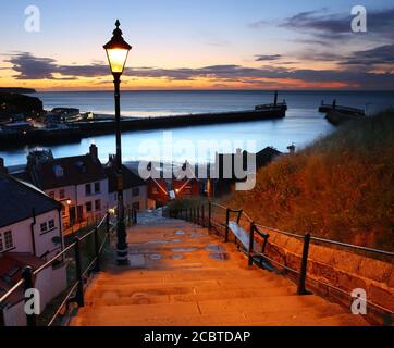 Image showing the 199 steps to whitby abbey after sunset with a street lamp and the harbour in the background. Whitby, North Yorkshire, England, UK. Stock Photo