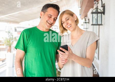 Middle age couple, woman and man using smart phone at the balcony. Daylight Stock Photo