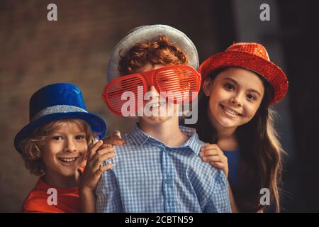 Three kids in party hats feeling happy and enjoyed Stock Photo