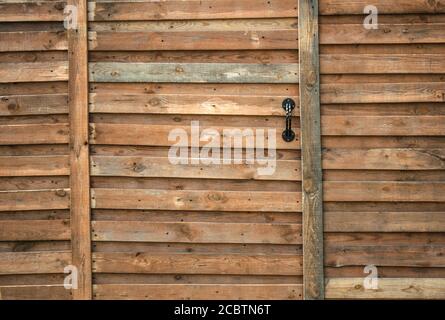 Part of a solid wooden fence with a door and a handle. The door is closed. The concept of reliability, security. Shot from the front Stock Photo