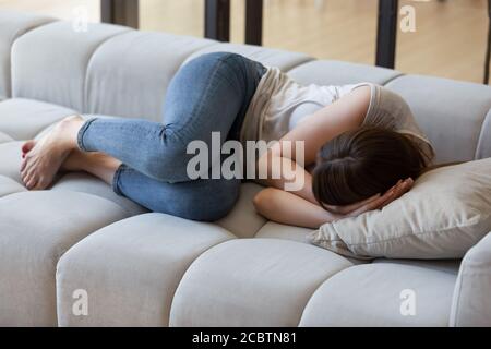 Frightened young woman curled up on sofa in fetal position