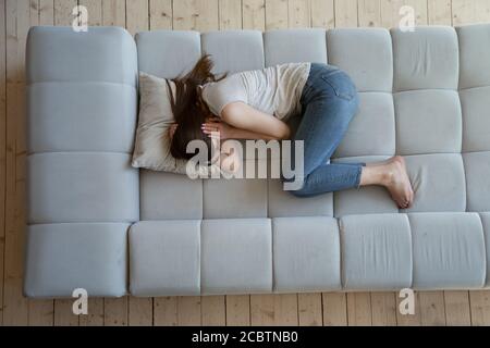 Distressed young female snuggling down on couch at home Stock Photo