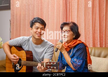 Adult son and senior mom sing a song while relaxed sitting on couch Stock Photo