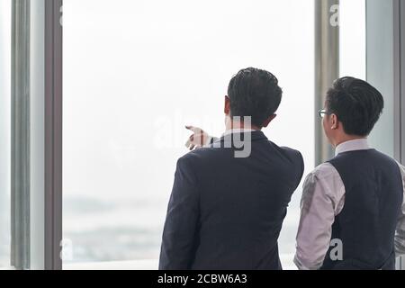 rear view of two asian business people standing in front of office window having a discussion Stock Photo