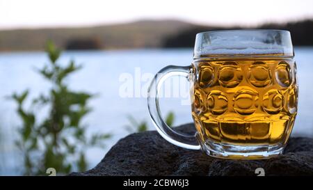 The midnight sun shines on a newly poured beer in a large pint glass. Photo was taken on midsummer's day next to the lake Siljan in Sweden. Stock Photo