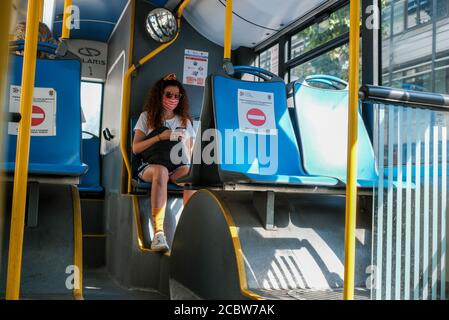 Belgrade / Serbia - August 8, 2020: Young girl wearing a medical face mask on Belgrade city public bus with posters warning to keep social distance on Stock Photo