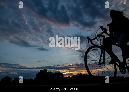 A cyclist rides with no hands on the handlebars through a London park at sunset Stock Photo