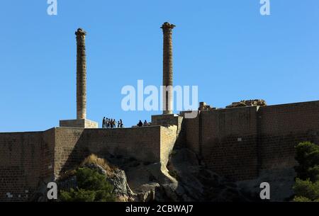 Tourists stand near the ancient stone columns which stand atop the Kale (castle) on Damlacik Hill  which overlooks Golbasi Park in Sanliurfa, Turkey. Stock Photo