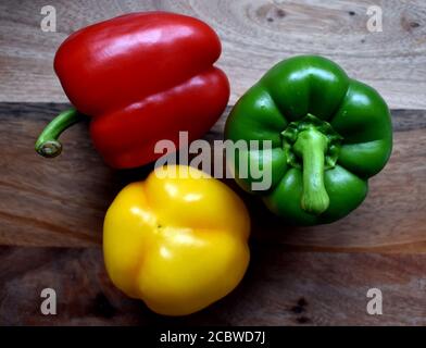 Sweet peppers, perfect skin, Red Green Yellow, Vibrant, attractive, yummy and enticing bunch on wooden chopping board under natural light. Stock Photo