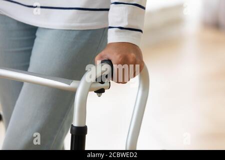 Older injured woman with walking equipment trying making steps. Stock Photo