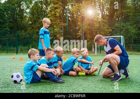 Young coach teaches little children the strategy of playing on football field.  Stock Photo