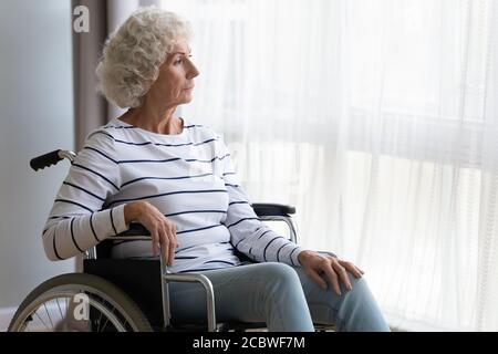 Thoughtful middle aged old hoary woman sitting in wheelchair. Stock Photo