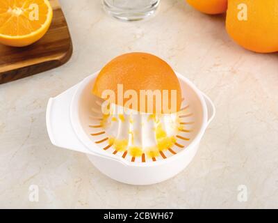 Half an orange on a plastic manual citrus juicer in the process of squeezing juice on a kitchen table. Vegetarian, raw food diet and healthy eating. Stock Photo