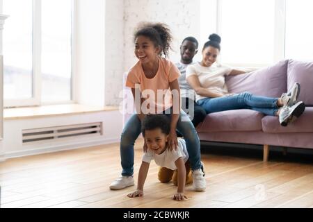 Happy married couple watching their children playing leapfrog on floor Stock Photo