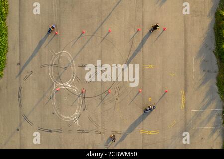 top down wide aerial view of four riders having fun on an advanced motorcycle training slalom course between orange cones with long shadows, painted Stock Photo