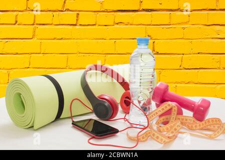 dumbbells, Mat, smartphone and earphones on yellow brick wall background Stock Photo