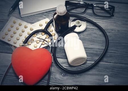 A heart with a stethoscope lies on a wooden background. Healthy heart Stock Photo