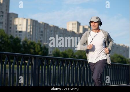 Mature Caucasian man with headphones jogging in the city Stock Photo