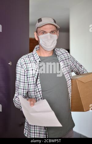 Delivery man in medical face mask with a box in the doors Stock Photo