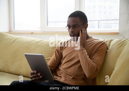 Amazed african american man reading shocking news on tablet screen Stock Photo
